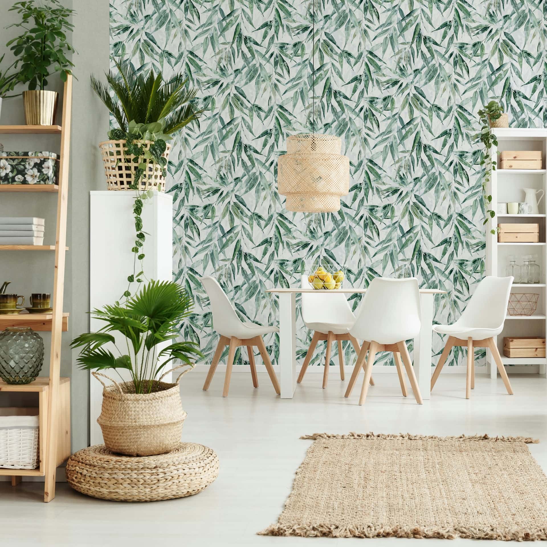 Marburg Naomi 89039 Green leafy botanical wallpaper behind a white dining table and chairs with a woven pendant light, shelves, rug, and indoor plants.