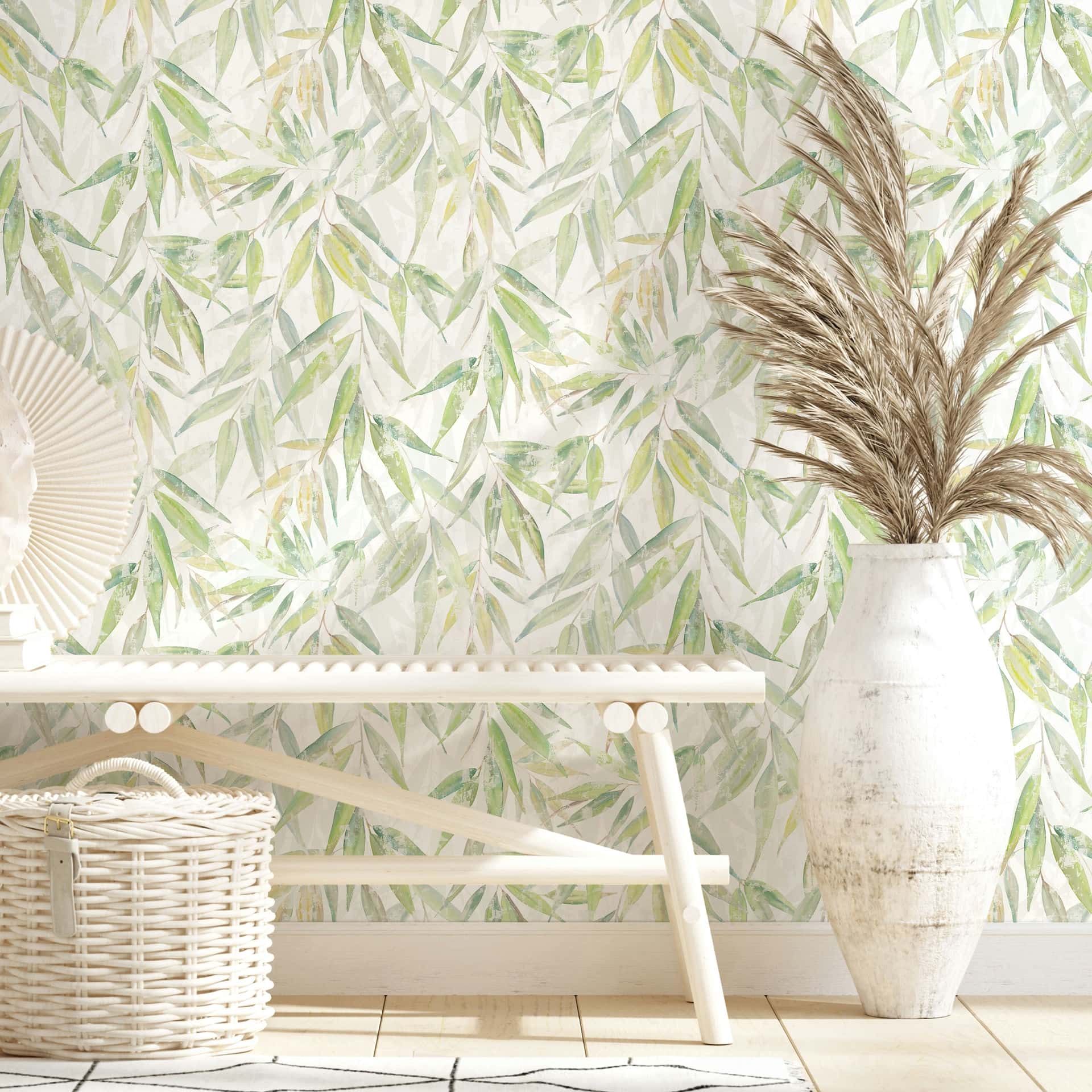 Marburg Naomi 89041 Watercolor-style green leaf wallpaper on a light background, shown behind a light wood bench, a wicker basket, and a tall white vase with pampas grass.