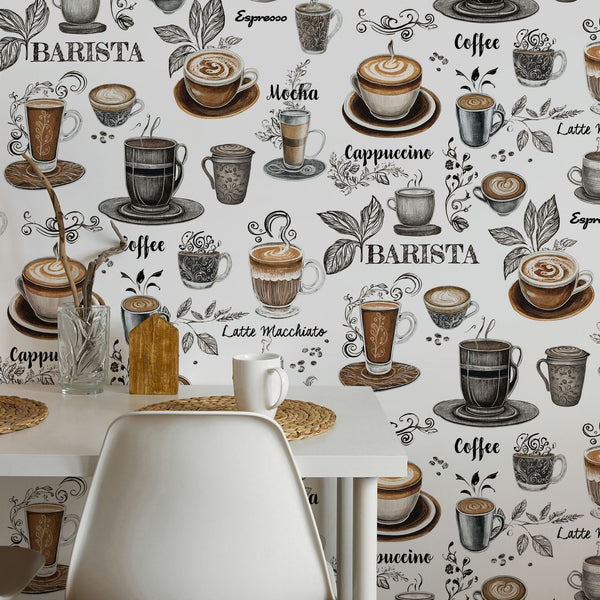 Marburg Naomi 89043 Coffee-themed wallpaper with illustrated cups, mugs, beans, and coffee names in brown and gray on a white background. In front is a white dining table with a white mug, woven placemats, a clear glass holding branches, a small wooden board, and a white chair.