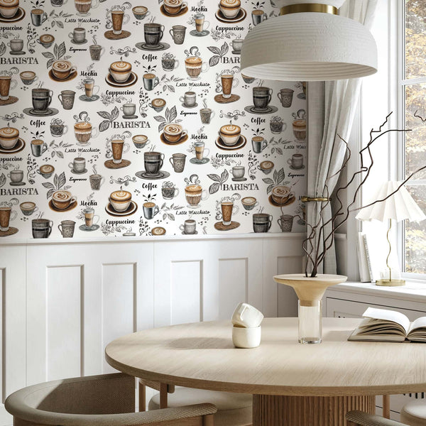 Marburg Naomi 89043 Dining nook with white coffee-themed wallpaper featuring hand-drawn cups, mugs, beans, leaves, and coffee names in brown and black above white wainscoting; round wood table, pendant light, window with curtains, a vase with branches, and a table lamp.