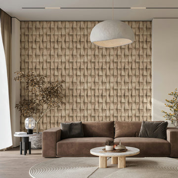 Marburg Novamur Mona 81648 Beige wallpaper with a repeating 3D geometric fold pattern shown in a living room with a brown sofa, round coffee table, pendant light, side table with a glass lamp, and potted plants.