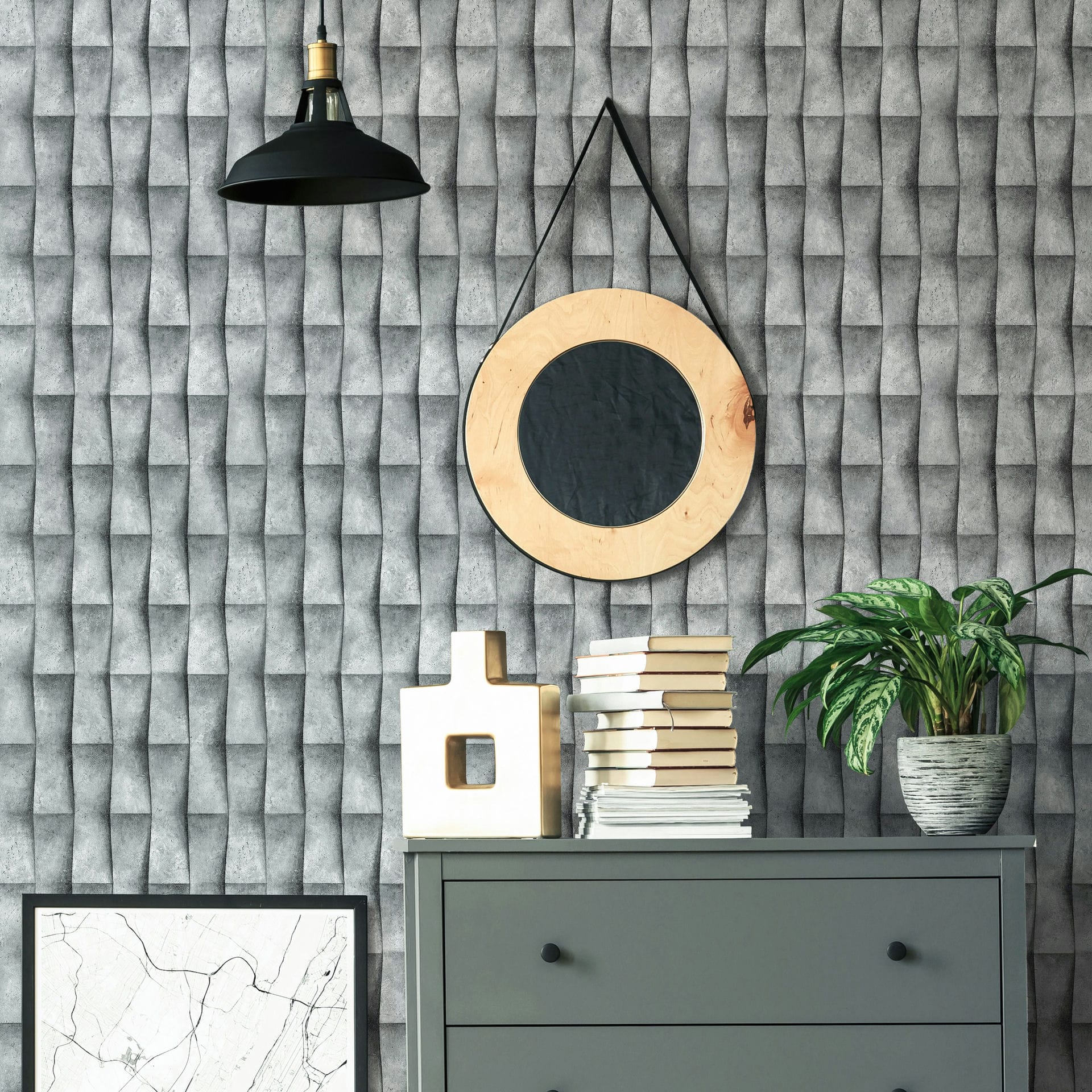 Marburg Novamur Mona 81649 Gray 3D‑effect geometric wallpaper shown behind a gray dresser styled with stacked books, a sculptural object, a potted plant, a round hanging mirror, a framed print, and a black pendant light.