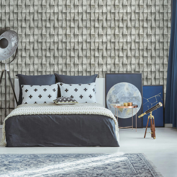 Marburg Novamur Mona 81651 Bedroom scene with a gray 3D geometric patterned wallpaper behind a made bed. A tripod floor lamp stands to the left, framed art leans on the floor beside a round metallic side table, a telescope on a wooden tripod sits to the right, with curtains and a rug in.