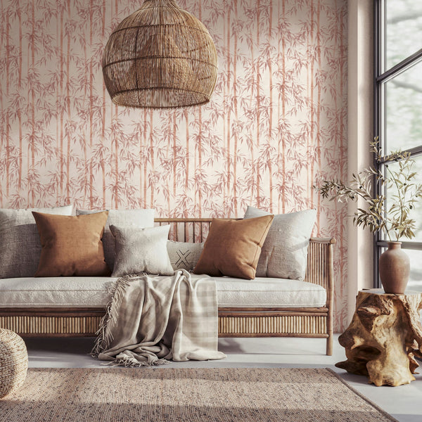 Marburg Novamur Mona 81670 Living room scene featuring bamboo-patterned wallpaper in warm orange on a light beige background. A wooden sofa with neutral pillows and a throw sits beneath a woven pendant; a stump side table with a ceramic vase and branches, a pouf, a textured rug, and a窓面.