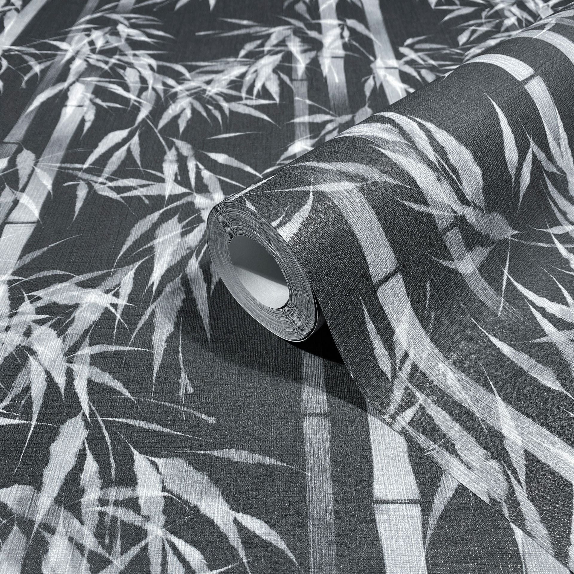Marburg Novamur Mona 81672 Close-up of a wallpaper roll on matching unrolled paper featuring a black and white bamboo pattern with stalks and leaves.