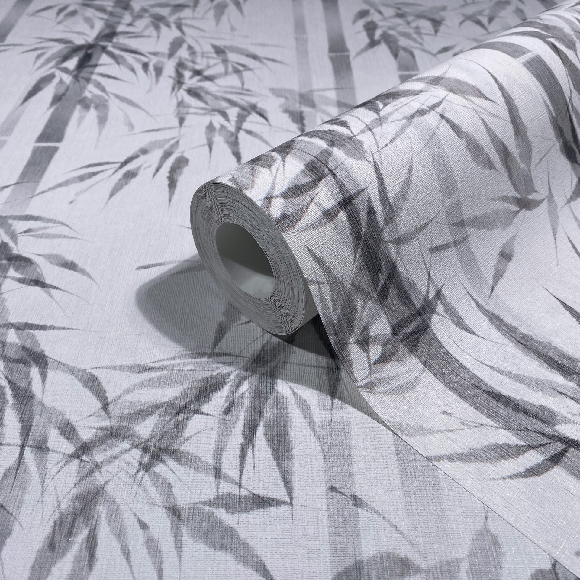 Marburg Novamur Mona 81673 Wallpaper roll with a grey bamboo leaf and stalk pattern on a light textured background, shown partially unrolled.