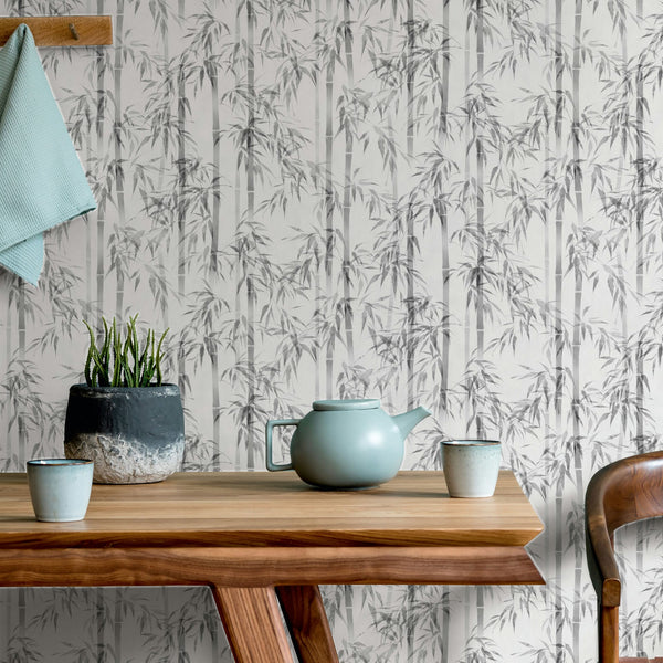 Marburg Novamur Mona 81673 Grey bamboo-patterned wallpaper behind a wooden table with a light green teapot, two cups, a potted plant, a wooden chair, and a cloth hanging from a wooden peg rail.