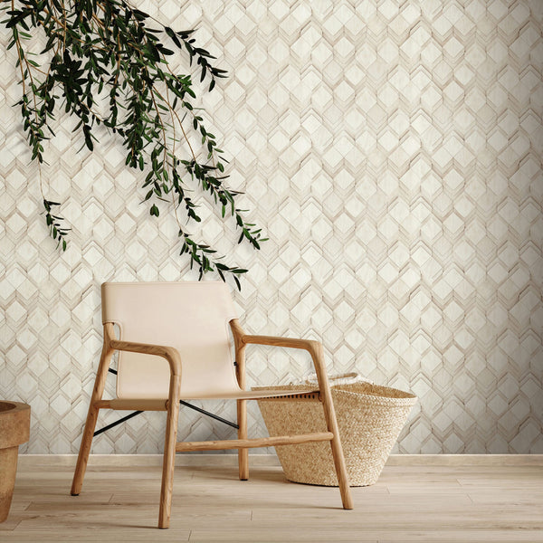 Marburg Novamur Mona 81678 Beige and white geometric chevron wallpaper shown as a feature wall behind a light wood chair, a woven basket, and a hanging leafy branch on a wood floor.