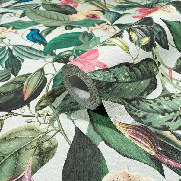 Marburg Novamur Mona 81684 Close-up of a wallpaper roll resting on an unrolled sheet printed with a botanical pattern of large green leaves, pink flowers, and a small blue bird on a light background.