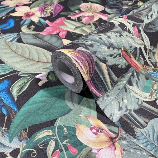 Marburg Novamur Mona 81685 Close-up of a wallpaper roll resting on matching paper, showing a dark-background tropical botanical design with large leaves, colorful flowers, and birds.