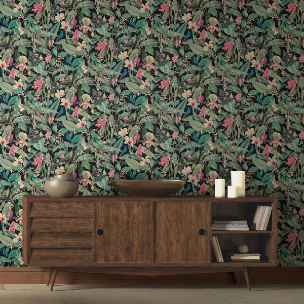Marburg Novamur Mona 81685 dense tropical botanical print with green leaves, pink flowers, and small birds on a dark ground wallpaper on a styled interior feature wall.