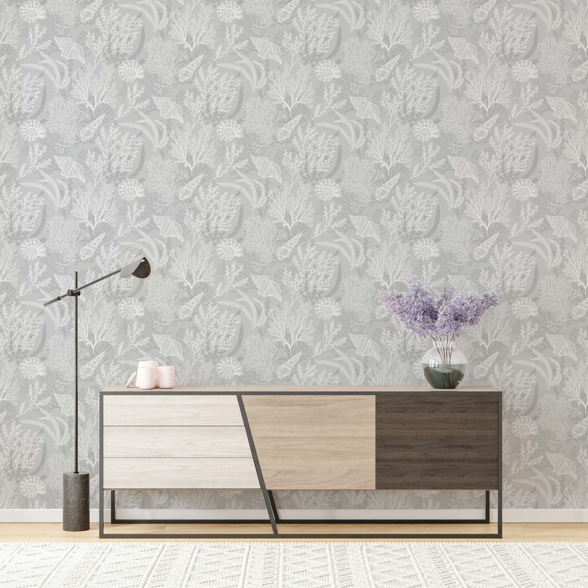 Marburg Novamur Mona 81687 Gray wallpaper with a tonal botanical foliage and seed head pattern shown in a room scene with a modern sideboard, a floor lamp, a glass vase of purple flowers, two small cups, a light rug, and baseboard trim.