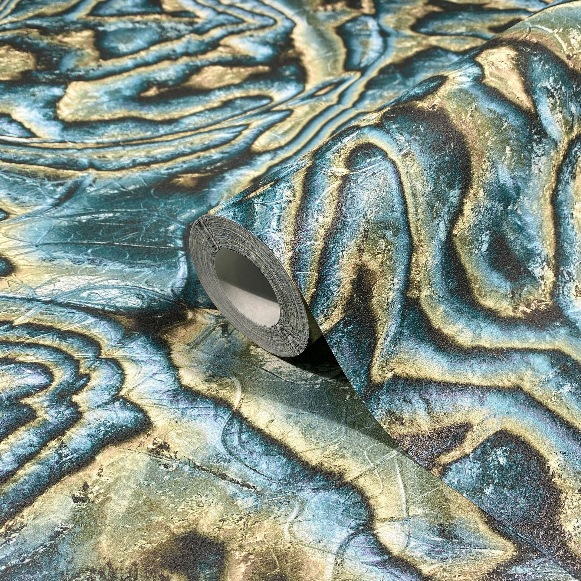 Marburg Novamur Mona 81692 A wallpaper roll resting on an unrolled sheet showing organic wavy bands in blue, green, and beige with a stone-like texture.
