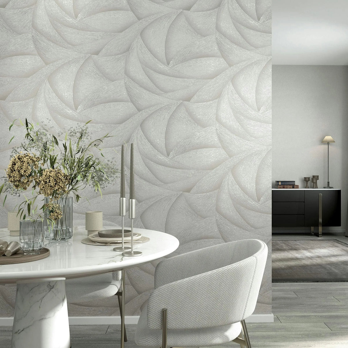 Marburg Ritus 35501 Abstract light beige and gray wallpaper with layered curved motifs, shown as a feature wall in a dining room with a round marble table, an upholstered chair, candlesticks, a vase with greenery, a sideboard, and a floor lamp.
