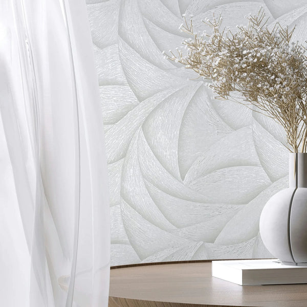 Marburg Ritus 35503 Tonal white wallpaper with overlapping curved, petal-like pattern. In front, a sheer curtain and a round table hold a white vase with delicate dried stems and a closed book.