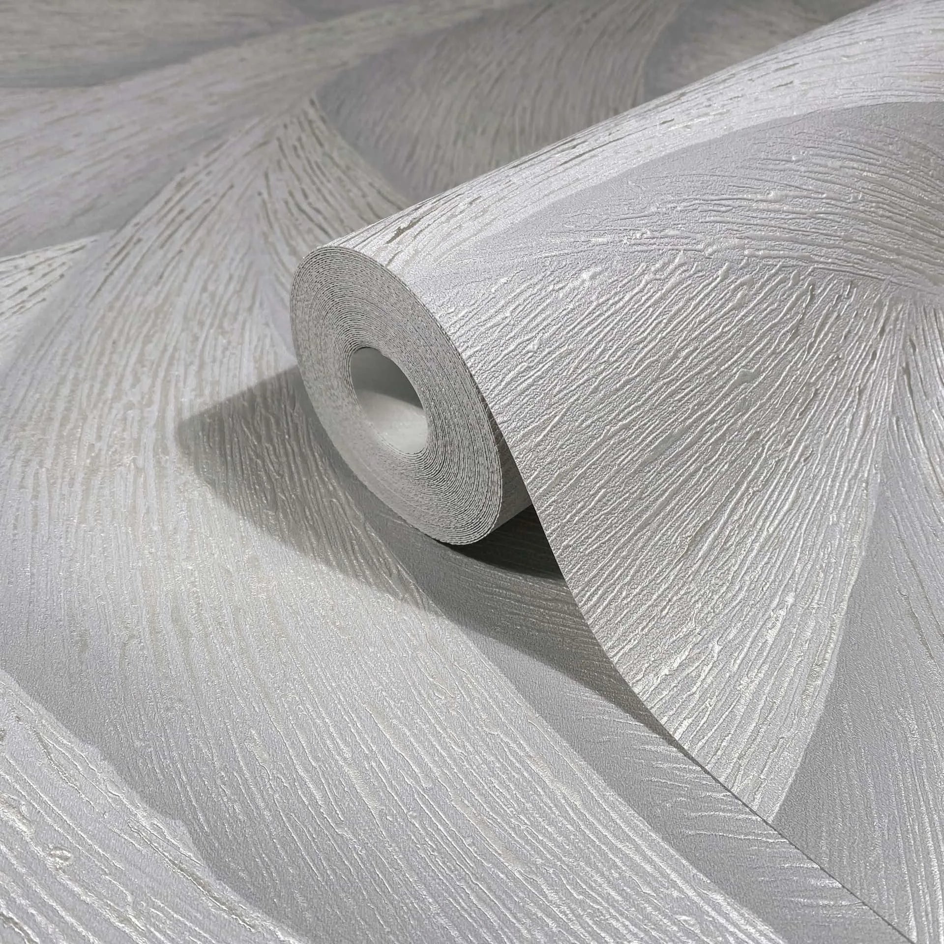 Marburg Ritus 35504 Close-up of a light gray wallpaper roll on matching unrolled wallpaper, showing a raised, sweeping striated texture with a slight sheen.
