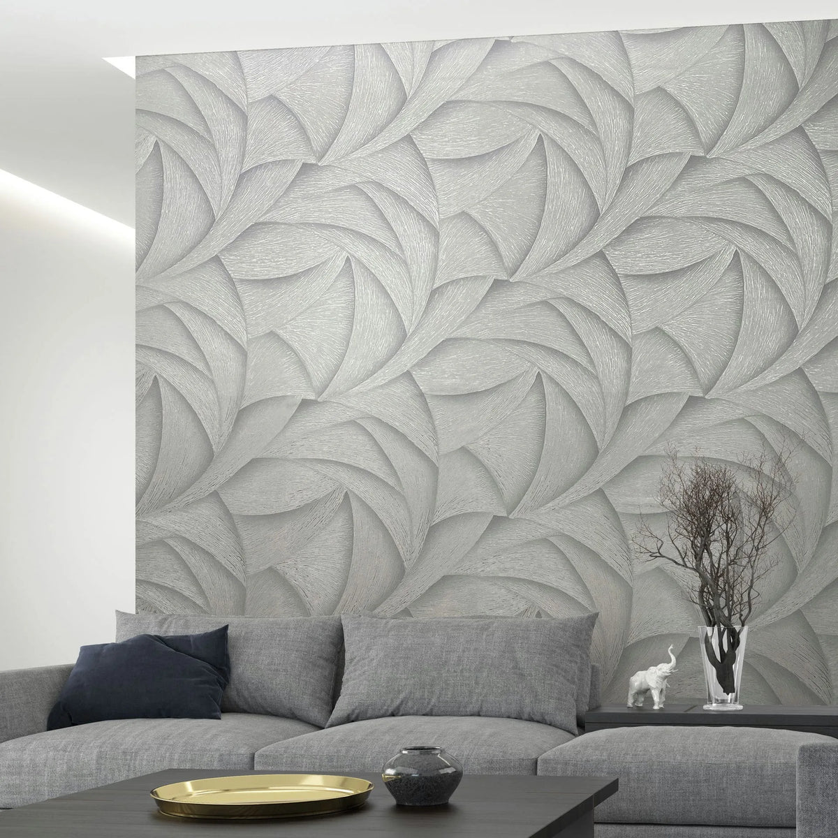 Marburg Ritus 35504 Room scene showing a gray wallpaper with an abstract layered curved pattern used as a feature wall behind a gray sectional sofa. A coffee table with a tray and small vase is in front, and a vase of branches with a small white elephant figurine sits on the low,.