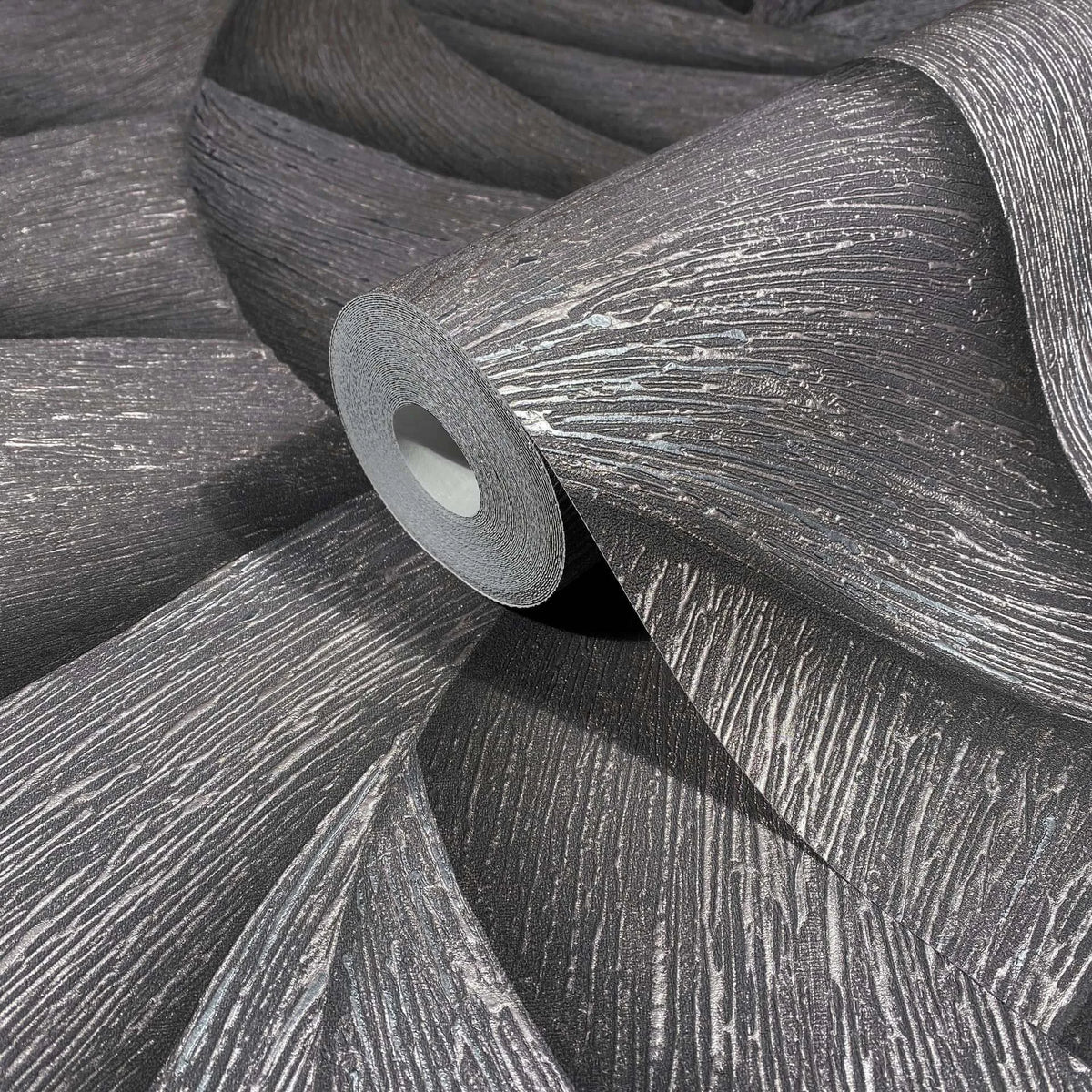 Marburg Ritus 35505 Close-up of a wallpaper roll resting on unrolled sheets, showing a dark ground with raised metallic striated texture.