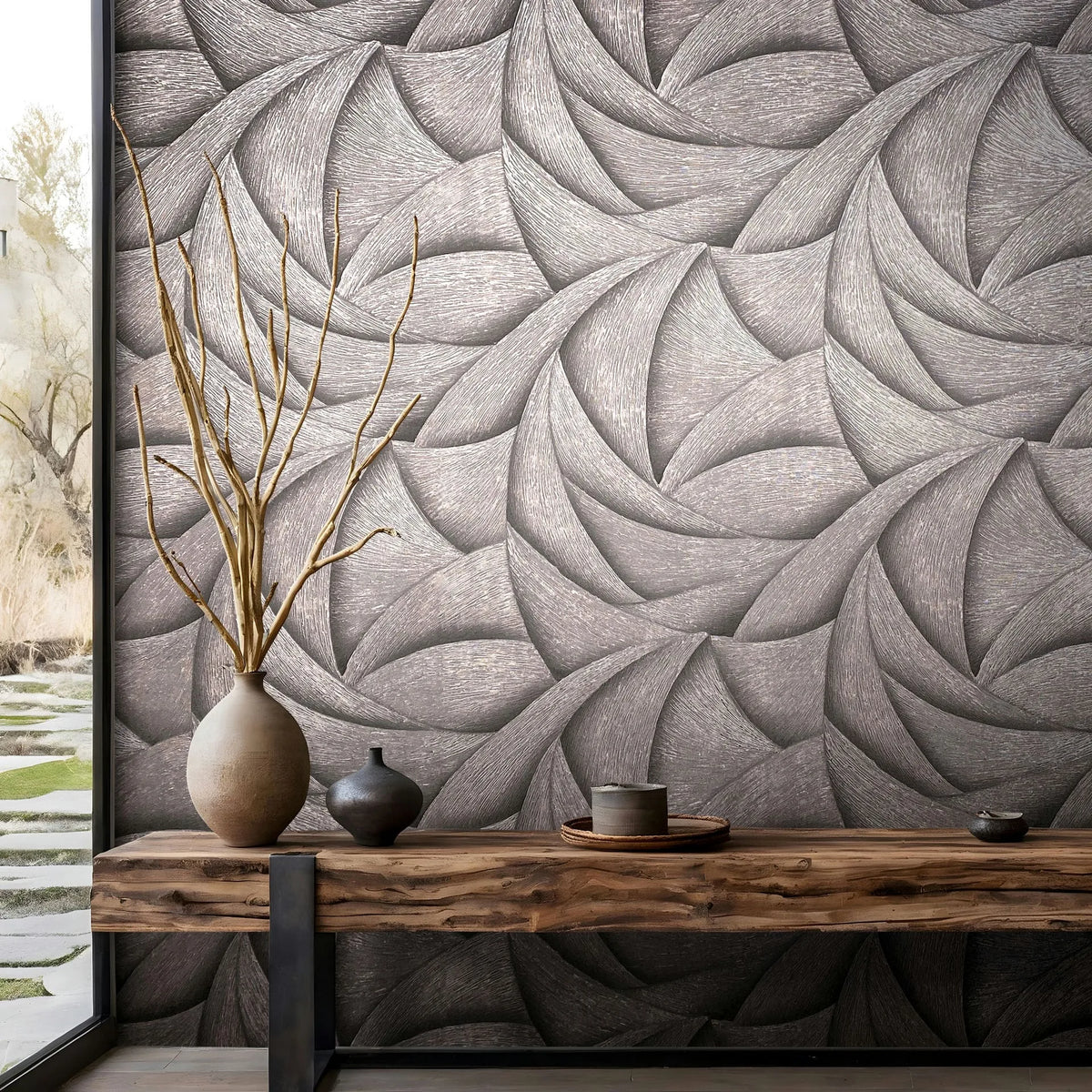 Marburg Ritus 35505 Textured swirl-pattern wallpaper with overlapping curved shapes in dark grey tones, shown behind a low wood bench holding ceramic vases with branches, a small vessel, and a tray beside a large window.