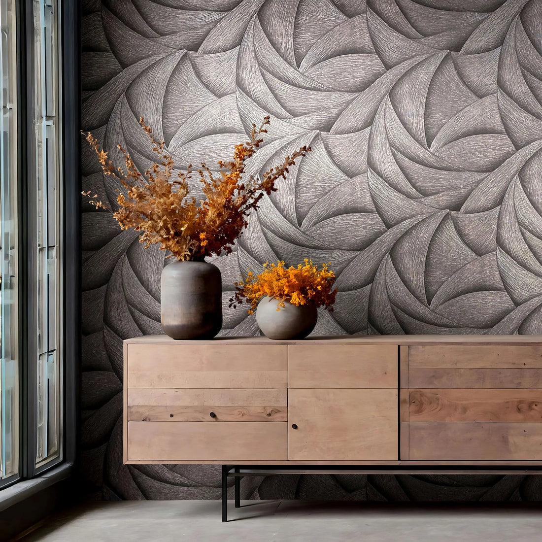 Marburg Ritus 35505 Abstract swirling pattern wallpaper in dark tonal shades behind a wooden sideboard with two vases of dried foliage, next to a tall window.