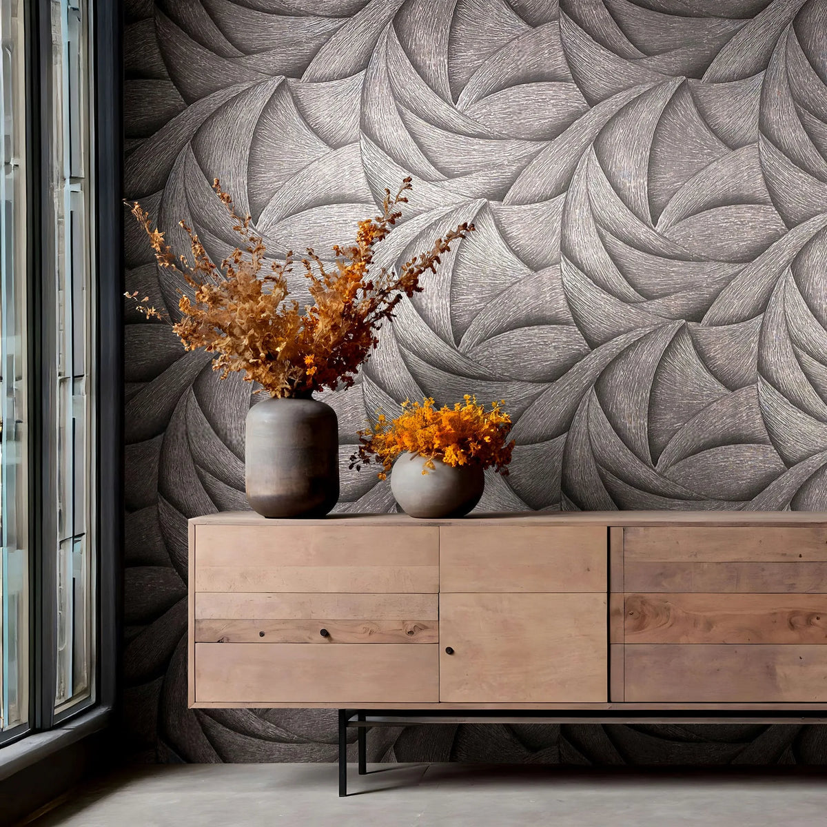 Marburg Ritus 35505 Abstract swirling pattern wallpaper in dark tonal shades behind a wooden sideboard with two vases of dried foliage, next to a tall window.