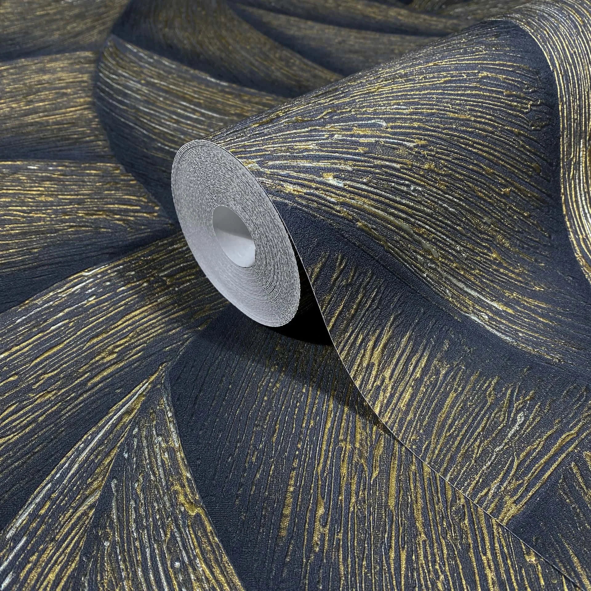 Marburg Ritus 35506 Close-up of a wallpaper roll on matching unrolled wallpaper, featuring a dark ground with sweeping gold streaks and textured lines.