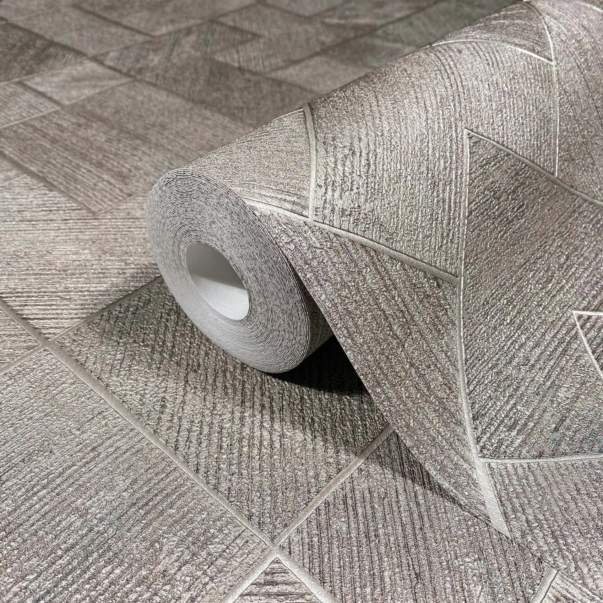 Marburg Ritus 35511 Close-up of a gray textured wallpaper roll on matching unrolled wallpaper, showing an angular geometric block pattern with ribbed detailing.