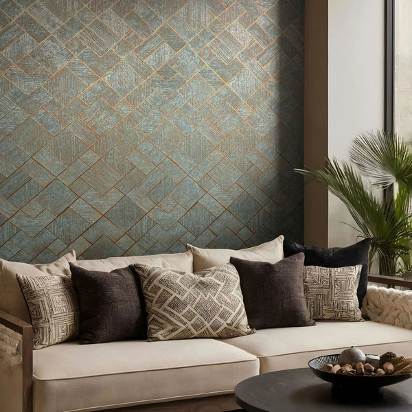 Marburg Ritus 35512 Blue wallpaper with a geometric herringbone pattern outlined in copper, shown behind a cream sofa with patterned cushions, a round coffee table with a bowl, and a potted palm near a tall window.