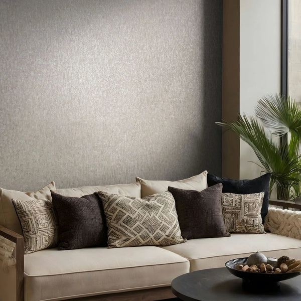 Marburg Ritus 35525 Textured gray wallpaper on a living room wall behind a beige sofa with patterned cushions, a palm plant by the window, and a round coffee table with a decorative bowl.