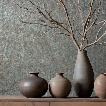 Marburg Ritus 35526 Textured blue and copper wallpaper behind a wood console with ceramic vases, including a tall vase holding bare branches.
