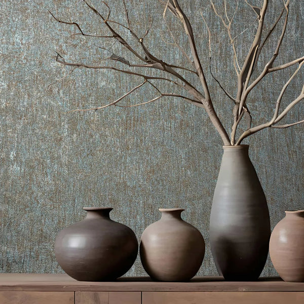 Marburg Ritus 35526 Textured blue and copper wallpaper behind a wood console with ceramic vases, including a tall vase holding bare branches.