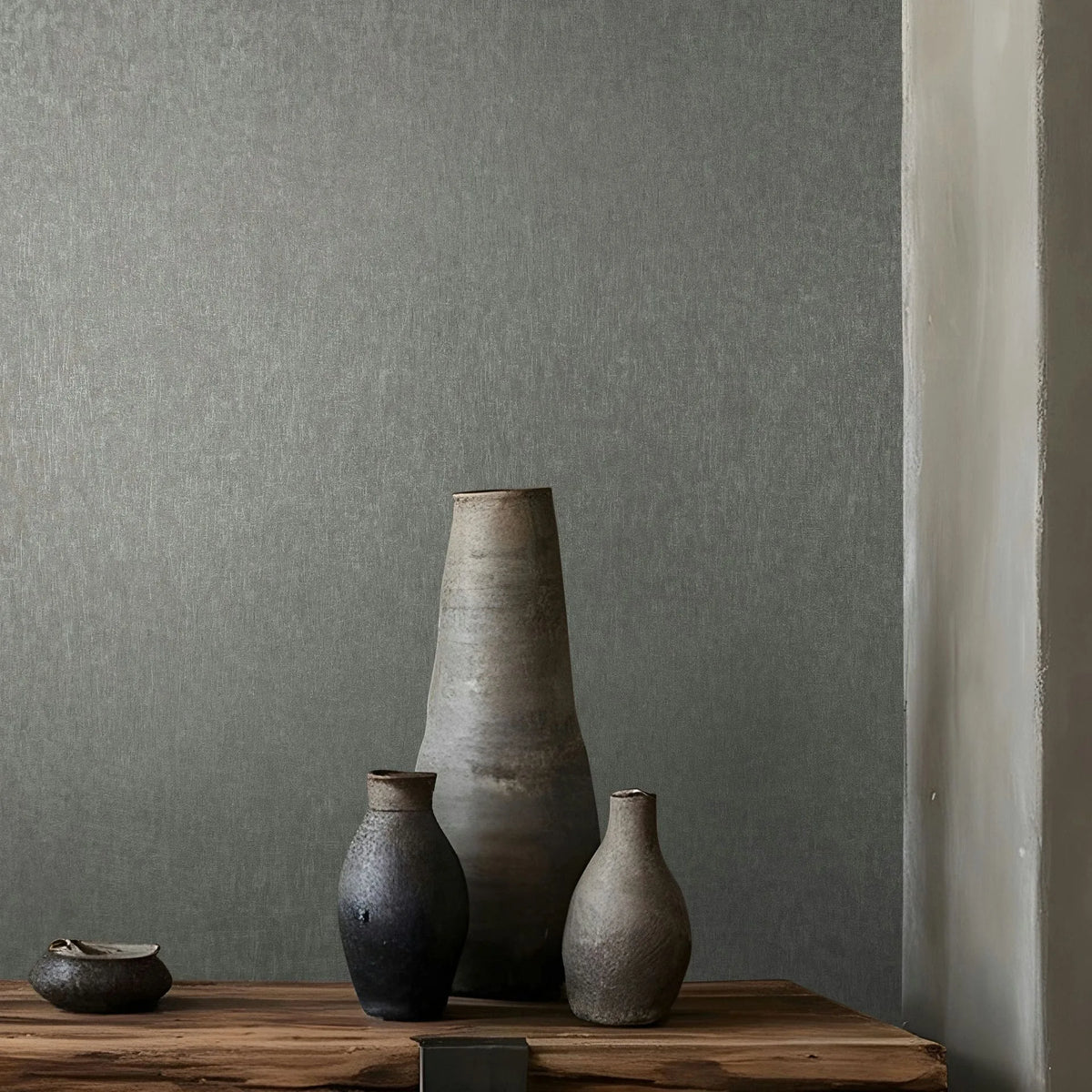 Marburg Ritus 35528 Gray textured wallpaper serves as a backdrop to a rustic wooden surface holding several ceramic vases and a small bowl, with a wall corner visible at right.