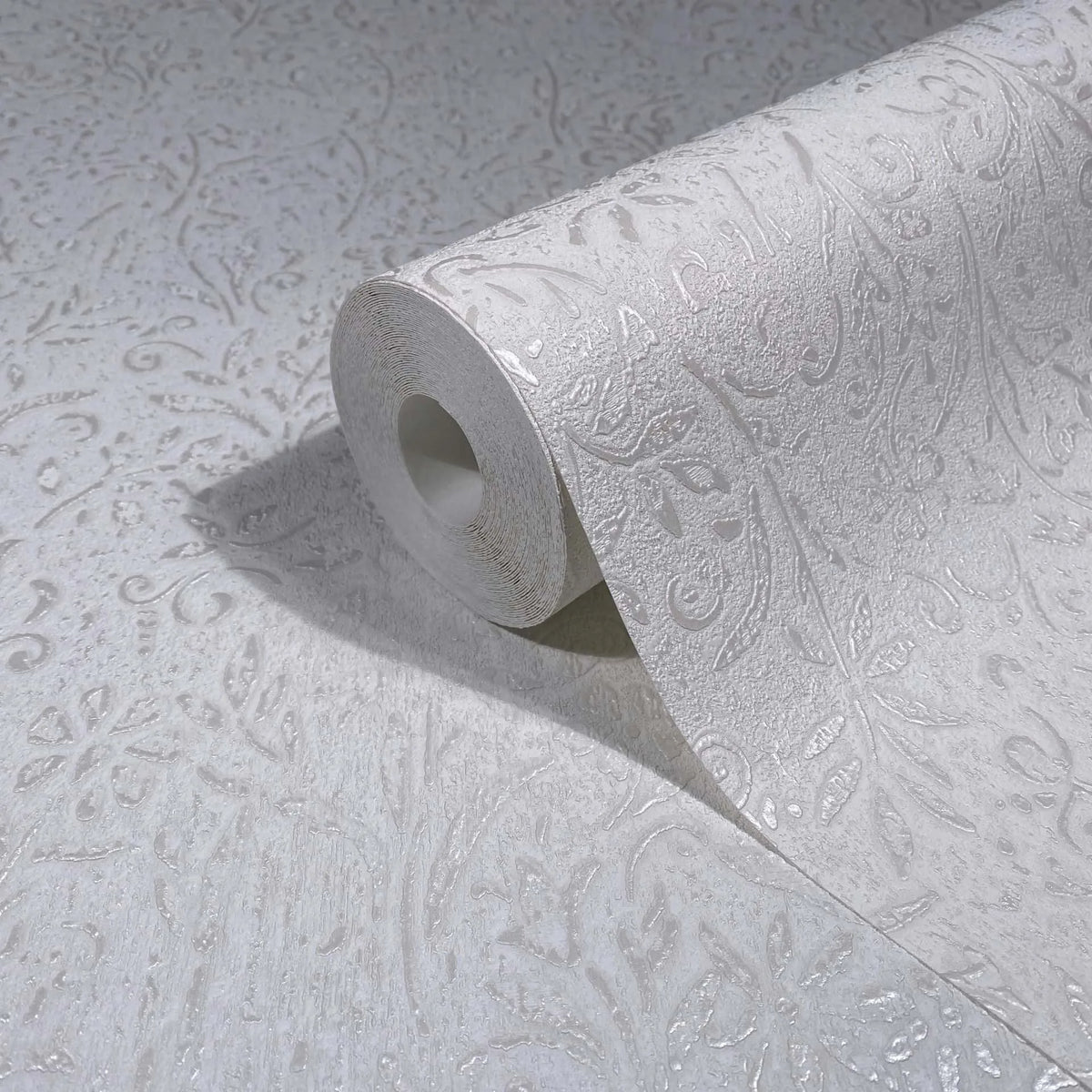 Marburg Ritus 35530 White textured wallpaper roll partially unrolled on a matching surface, showing a raised scroll and leaf pattern.