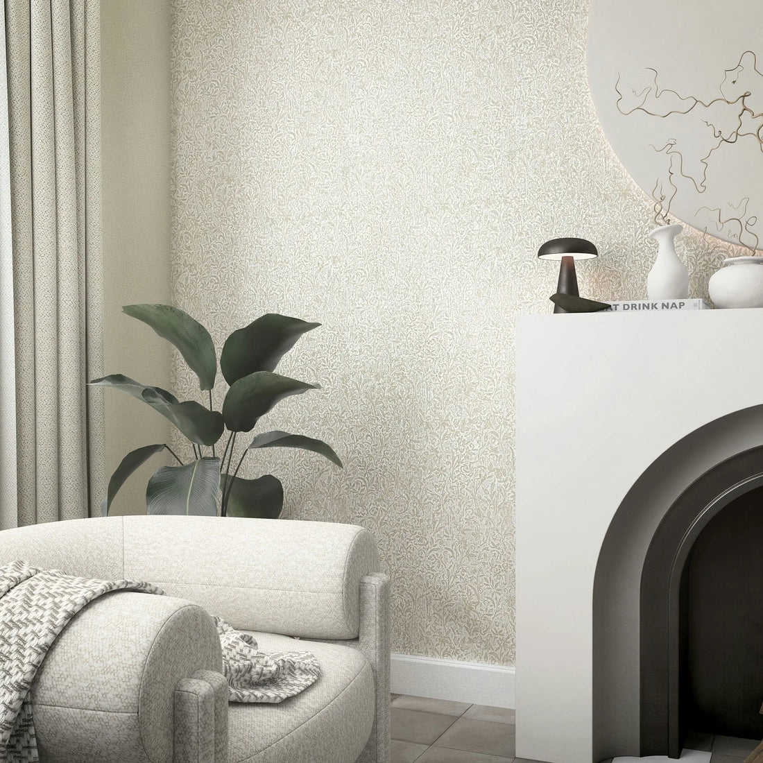 Marburg Ritus 35531 Beige wallpaper with a small leafy vine pattern shown in a living room scene with a white arched fireplace, a curved upholstered chair with a throw, a tall potted plant, and light curtains.