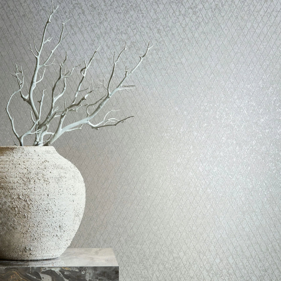 Marburg Ritus 35536 Light gray wallpaper with a small diamond lattice pattern; a large rough-textured vase with bare branches sits on a stone pedestal at the left.