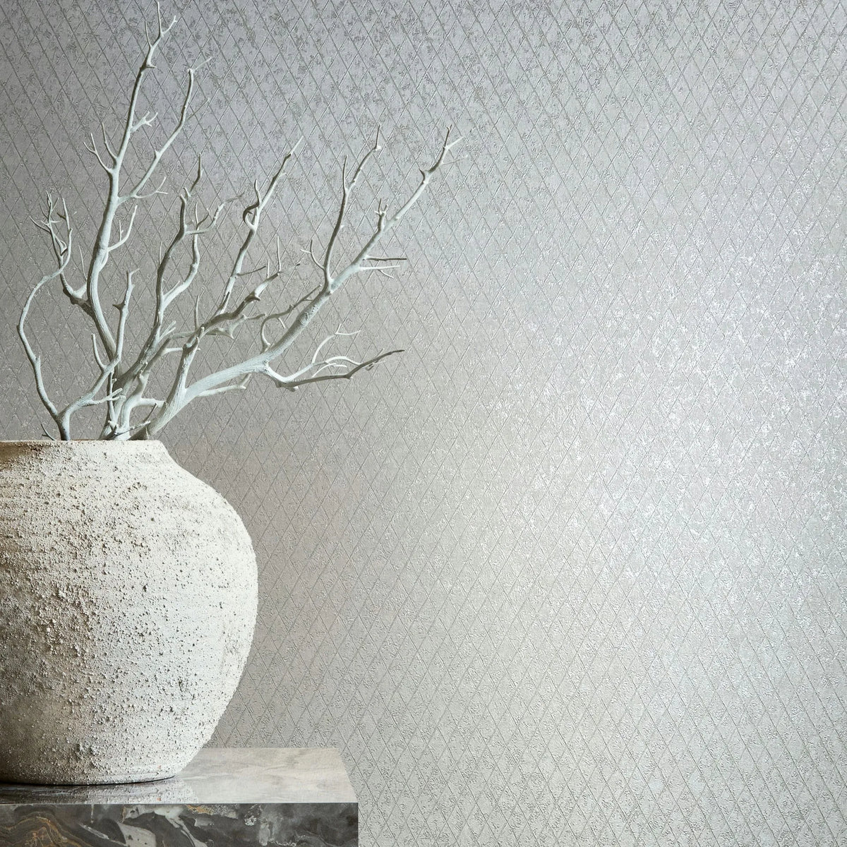 Marburg Ritus 35536 Light gray wallpaper with a small diamond lattice pattern; a large rough-textured vase with bare branches sits on a stone pedestal at the left.