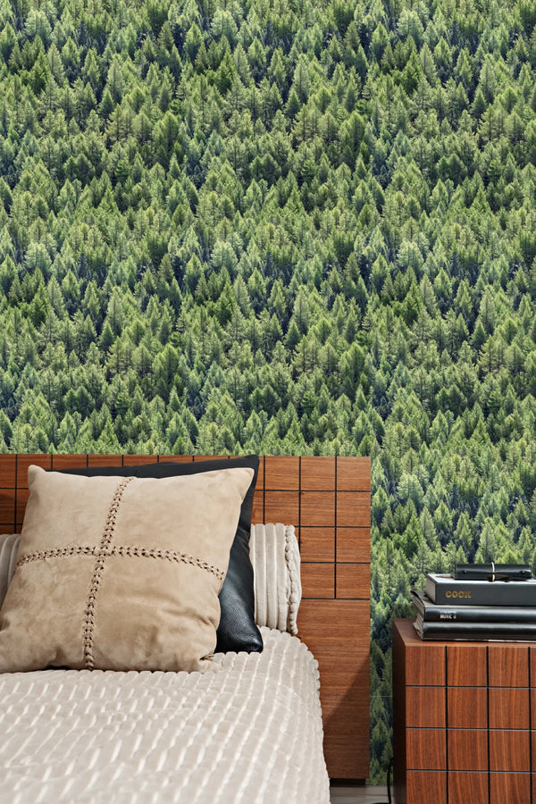 Marburg Struktura 45730 Green forest treetop wallpaper behind a bed with a wood headboard and a small nightstand stacked with books.