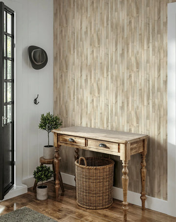 Marburg Struktura 45734 Beige wallpaper with a vertical wood‑plank effect is shown on an entry wall behind a wood console table, with a wicker basket below, two potted plants on a stool and the floor, a wall hook with a hat, and a glass‑paneled door.