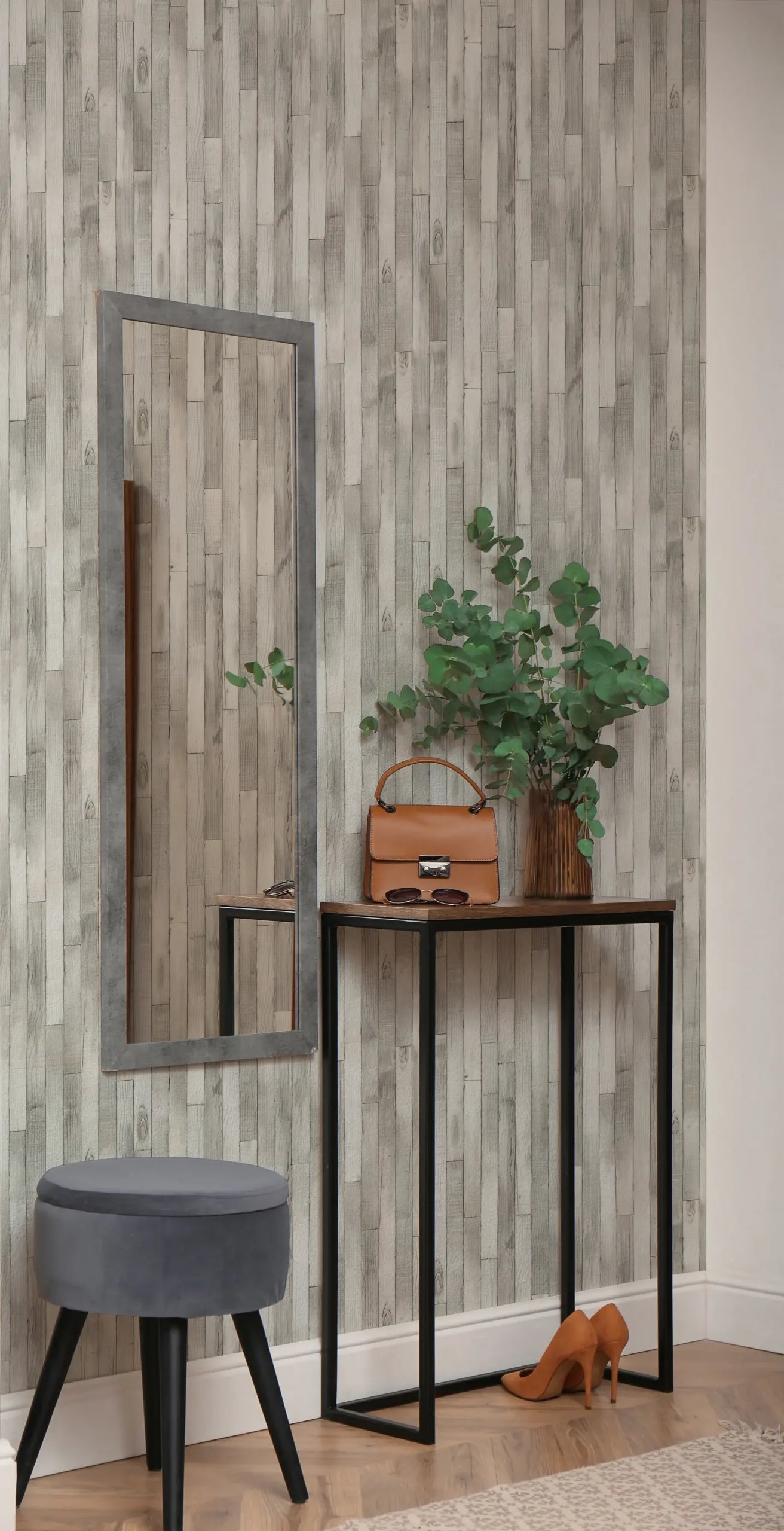 Marburg Struktura 45735 Gray wood plank effect wallpaper behind a slim console table with a mirror, a vase with green branches, a tan handbag, sunglasses, a gray stool, and a pair of tan heels on a wood floor.