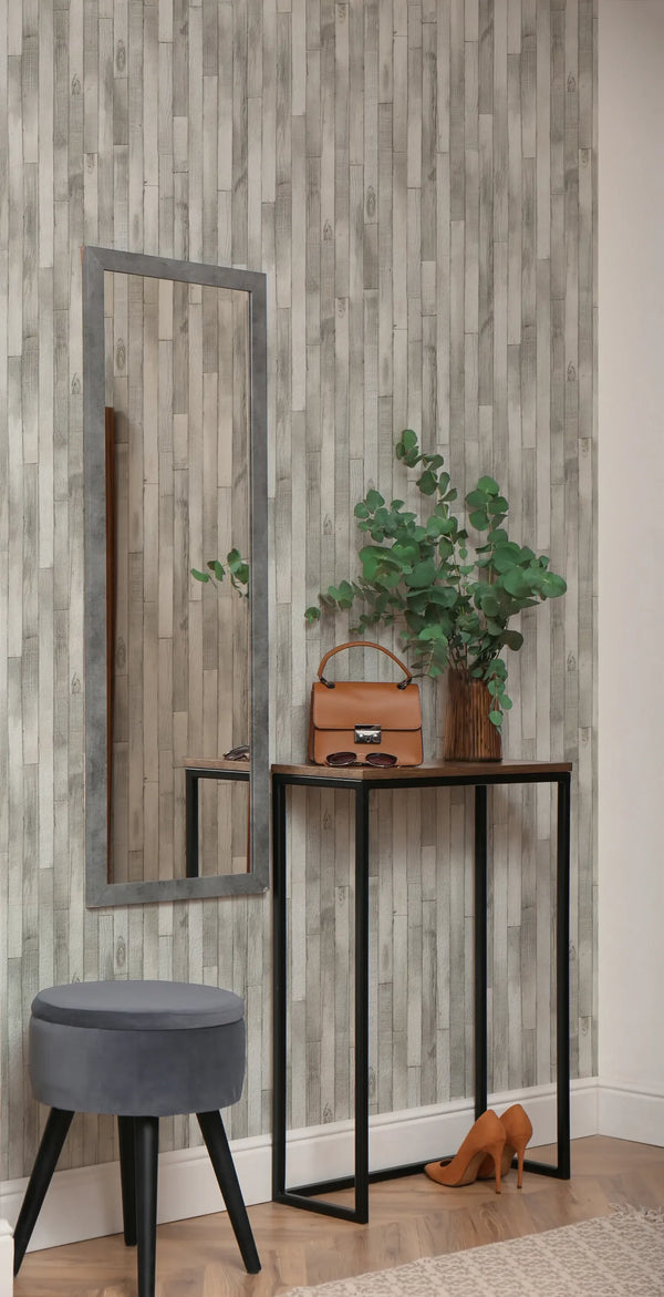 Marburg Struktura 45735 Gray wood plank effect wallpaper behind a slim console table with a mirror, a vase with green branches, a tan handbag, sunglasses, a gray stool, and a pair of tan heels on a wood floor.