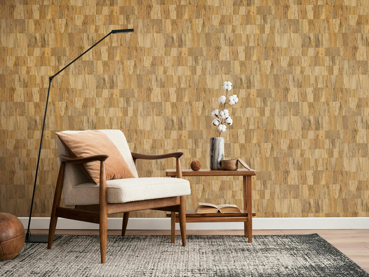 Marburg Struktura 45737 Living room scene with beige patchwork wallpaper of small rectangular blocks behind a mid-century armchair, slim floor lamp, and a wooden side table with a vase and books on a rug.