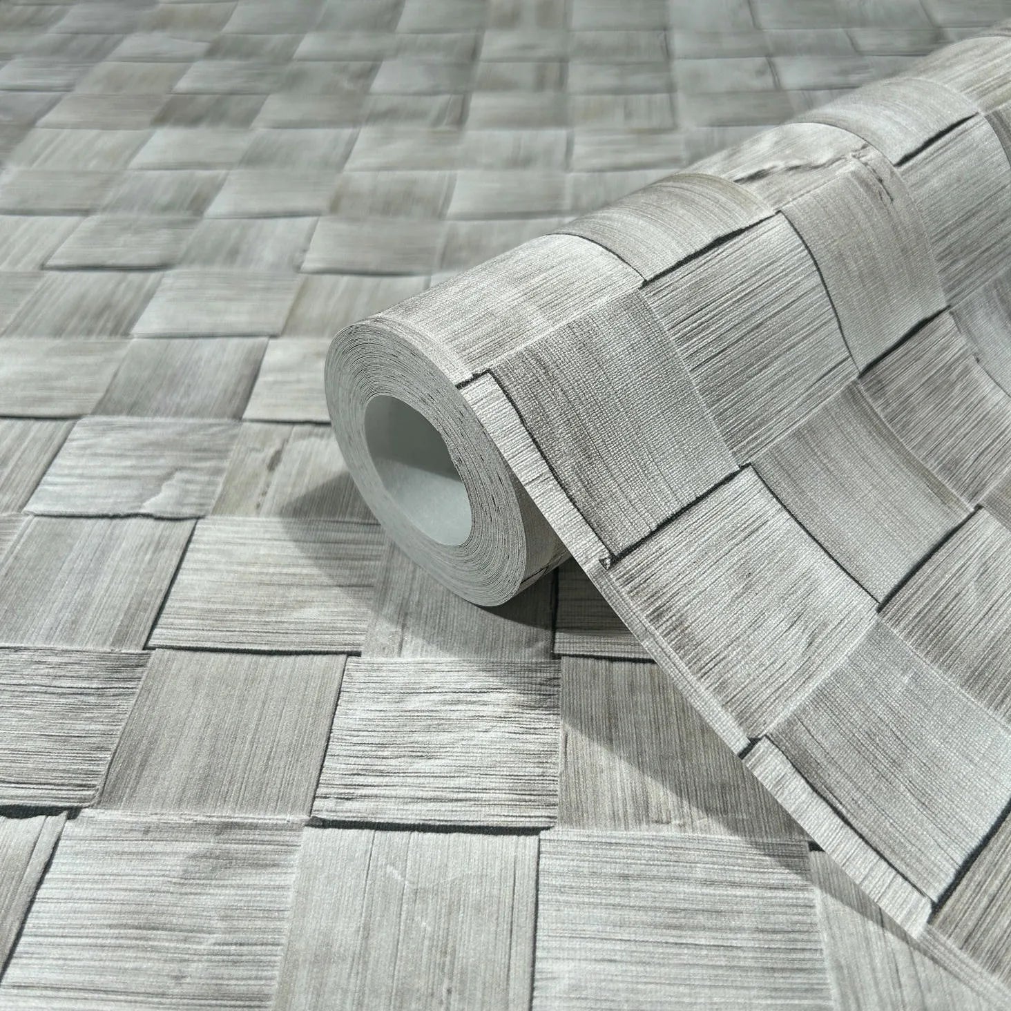 Marburg Struktura 45741 A wallpaper roll rests on matching gray wallpaper featuring a woven square pattern with fine linear texture.