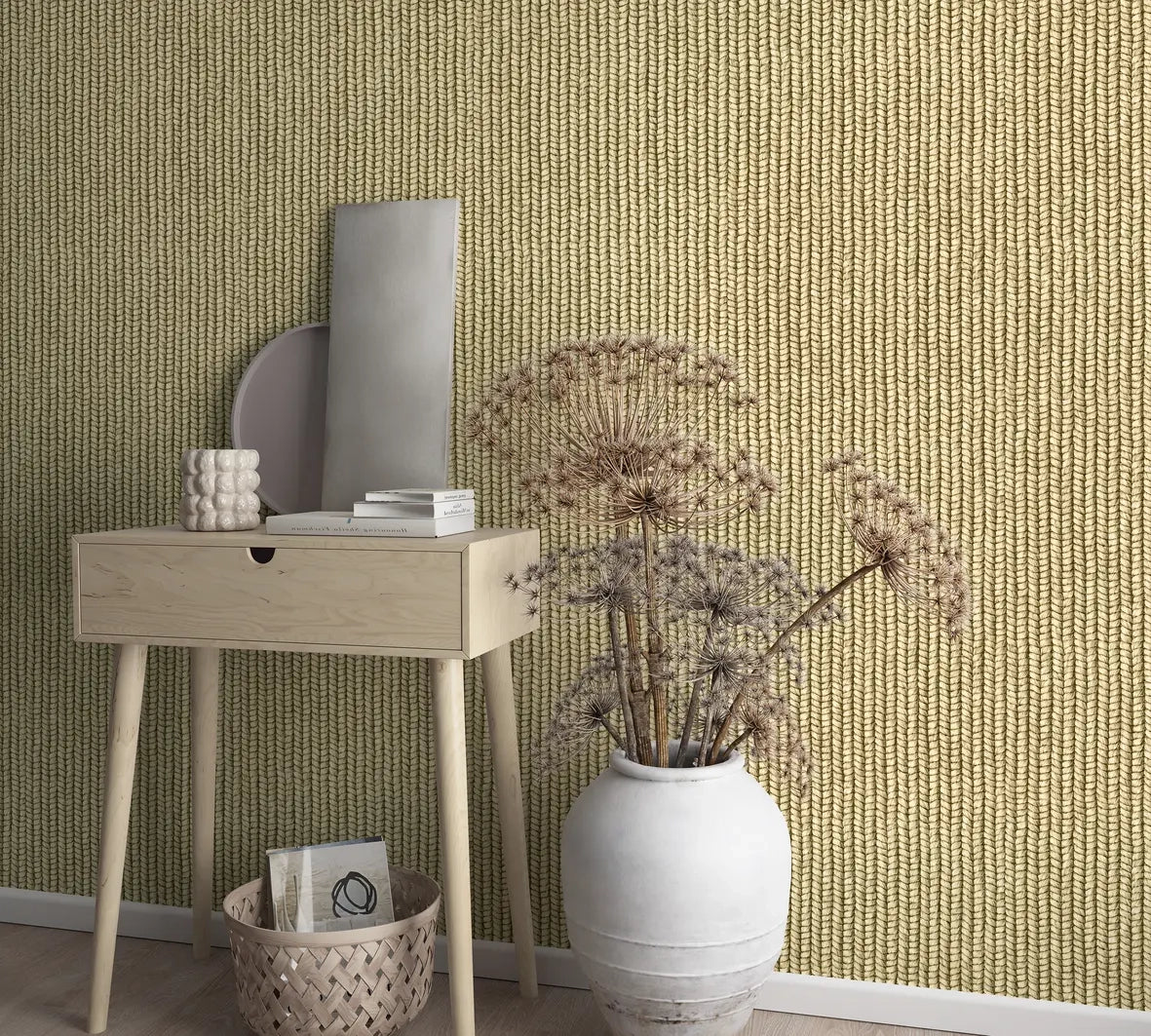 Marburg Struktura 45750 Beige-brown wallpaper with a vertical braided rope pattern behind a light wood console table with books and a small sculptural cup, a round and a rectangular panel leaning on the wall, a woven basket below with a booklet, and a large white vase holding dried,.