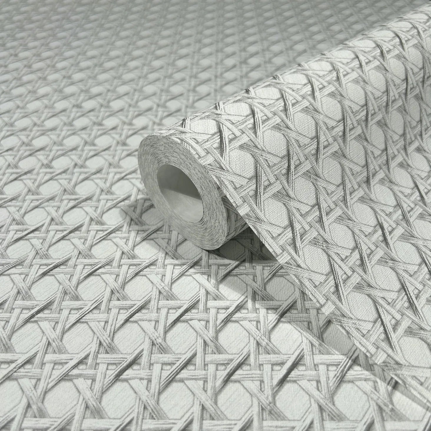 Marburg Struktura 45754 Close-up of a wallpaper roll resting on matching paper, showing a gray and white interlaced lattice pattern with diamond shapes.
