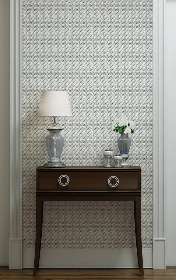 Marburg Struktura 45754 Gray and white small-scale geometric wallpaper behind a dark wood console table with a glass table lamp, a vase of white flowers, and small silver decor, framed by white wall molding.