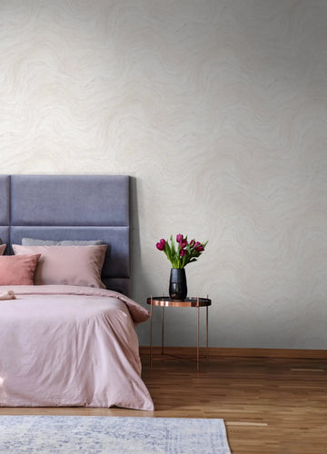 Marburg Struktura 45756 Light gray wallpaper with a soft wavy pattern behind an upholstered bed. A round metal side table holds a vase of flowers beside the bed, with a wood floor and part of a rug visible.