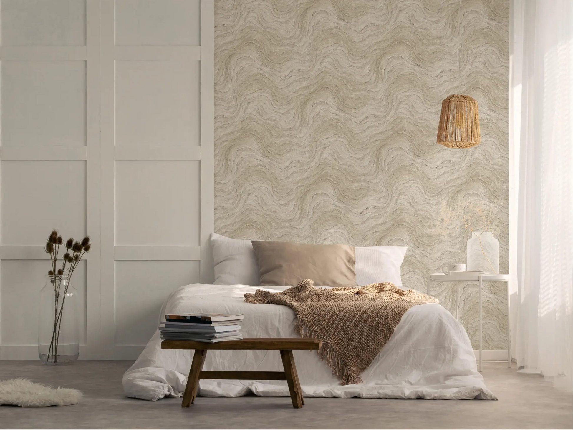 Marburg Struktura 45757 Bedroom scene showing a beige and gray wavy-pattern wallpaper used as a feature wall behind a low bed, with a rattan pendant light, small side table, and bench in view.