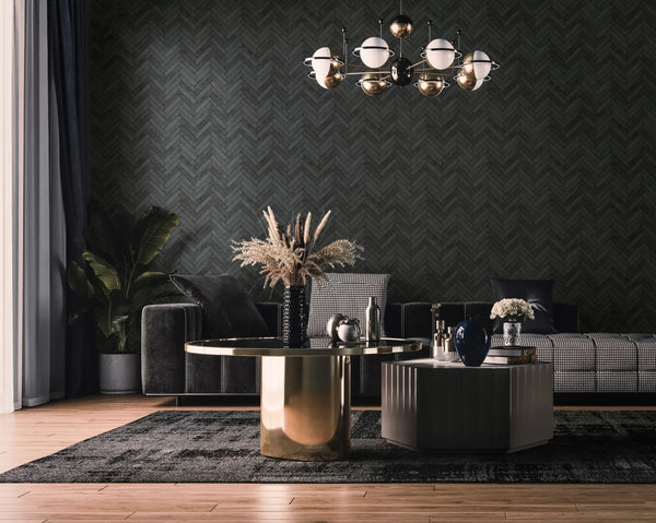 Marburg Struktura 45761 Dark herringbone-pattern wallpaper in anthracite on a living room feature wall, shown with a sofa, two coffee tables, a globe chandelier, curtains, a plant, and a dark rug.