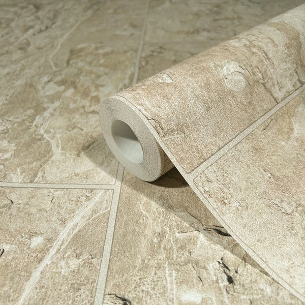 Marburg Struktura 45766 Close-up of a wallpaper roll printed with a beige stone tile pattern and grout lines, resting on matching unrolled wallpaper.