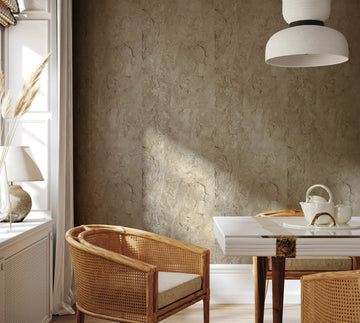 Marburg Struktura 45766 Beige stone-look block pattern wallpaper shown behind a dining setup with cane chairs, a white table, a pendant light, and a window with curtain at left.